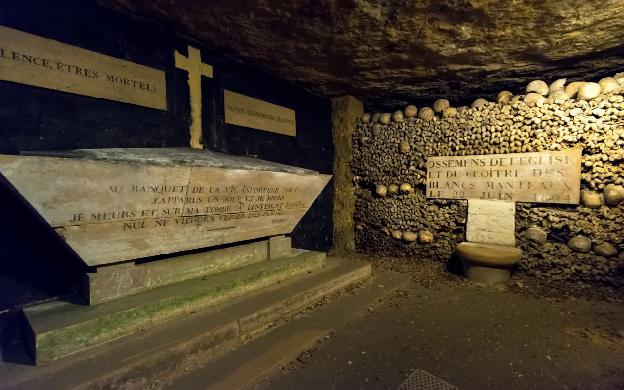 Underground view of the eerie Catacombs of Paris, with walls lined with skulls and bones.