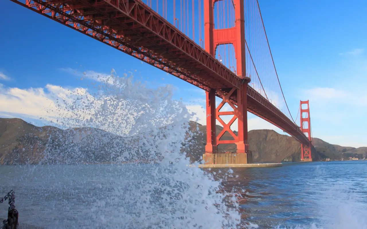 Golden Gate Bridge under a clear blue sky with waves splashing at the base
