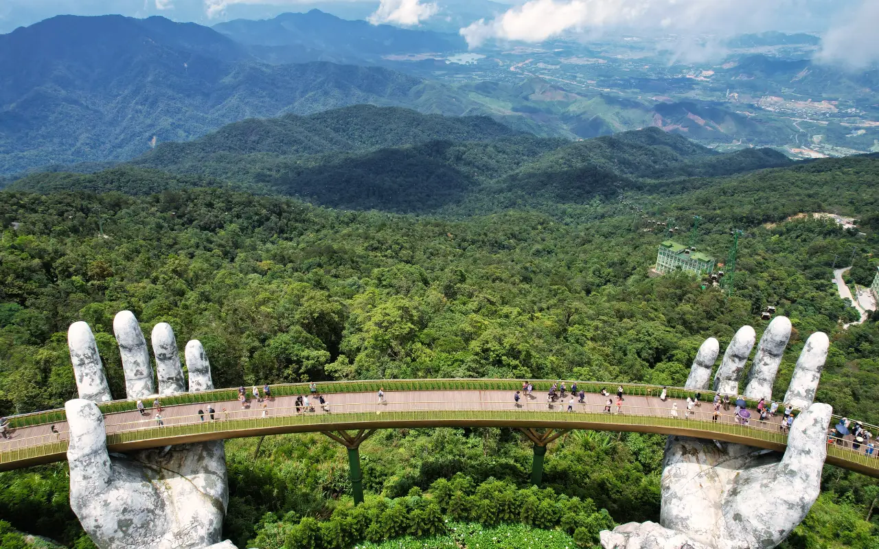 Aerial view of the Golden Hand Bridge held by giant stone hands amidst lush mountains