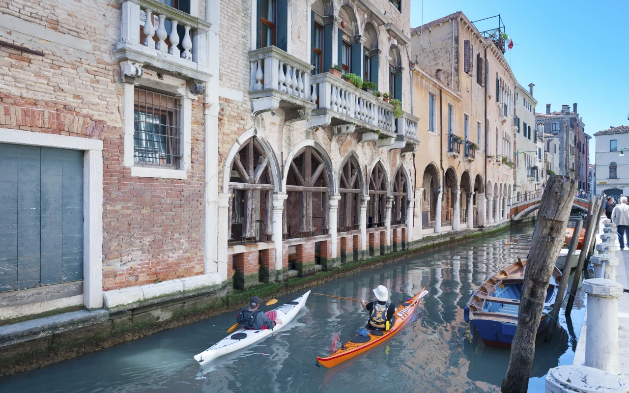 Kayaker skillfully navigating the picturesque canals of Venice with historic buildings in the background