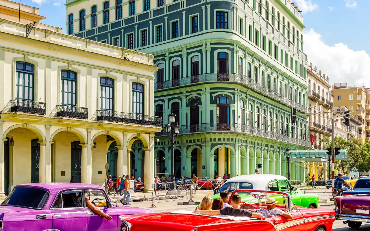 Colorful vintage cars driving through the streets of Old Havana, Cuba, with vibrant colonial buildings in the background.