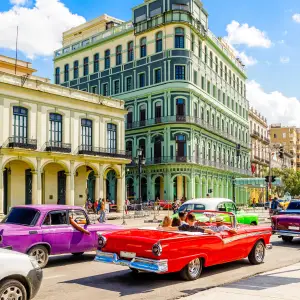 Colorful vintage cars driving through the streets of Old Havana, Cuba, with vibrant colonial buildings in the background.